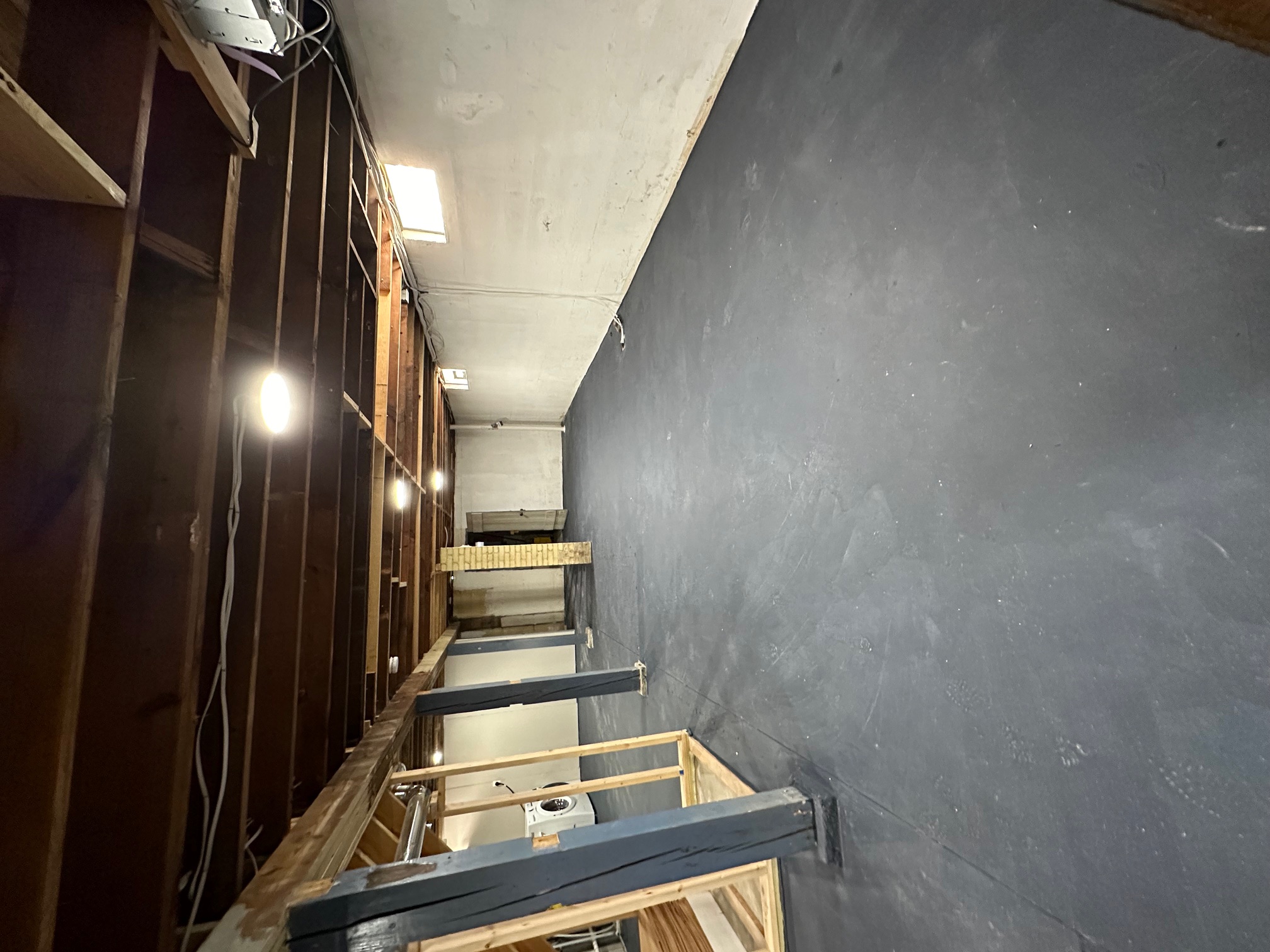 Basement looking down the length of the space — painted foundation walls, exposed joists overhead